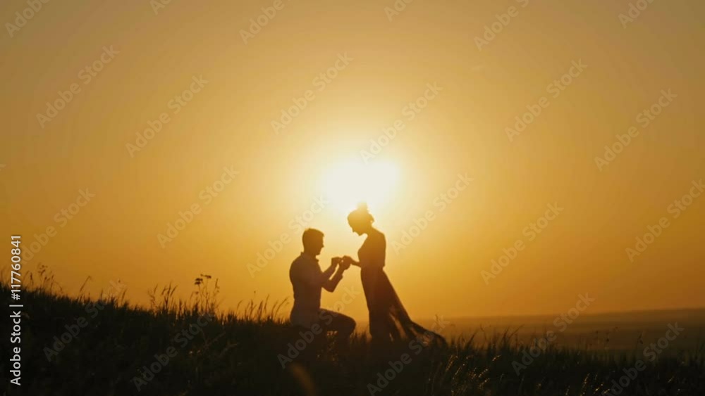 Romantic Silhouette of Man Getting Down on his Knee and Proposing to Woman on high hill - Couple Gets Engaged at Sunset - Man Putting Ring on Girl's Finger, slow motion Romantic Silhouette of Man Getting Down on his Knee and Proposing to Woman on high hill - Couple Gets Engaged at Sunset - Man Putting Ring on Girl's Finger, slow motion