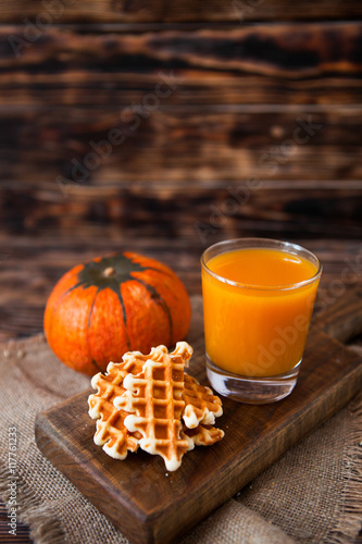 Glass of fresh pumpkin juice with wafer and pumpkin on dark wood