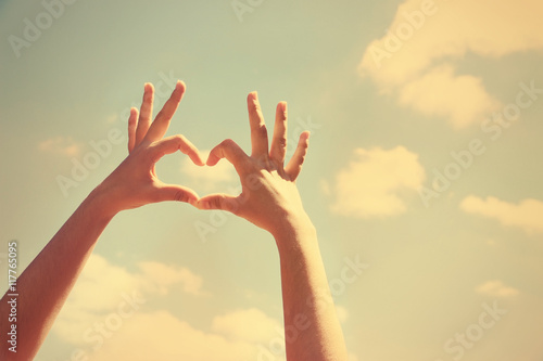 Young girl holding hands in heart shape framing on sky background