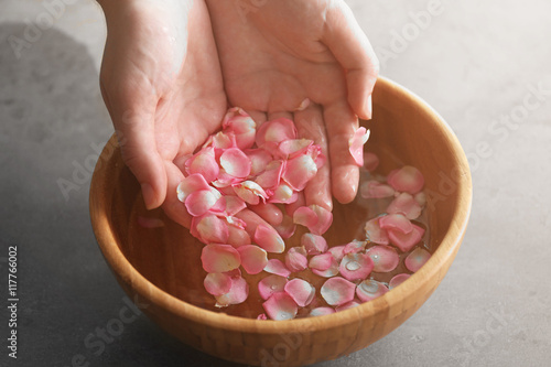 Hands in wooden bowl with petals and water