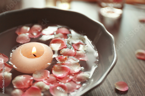 Petals in bowl with candle on wooden background