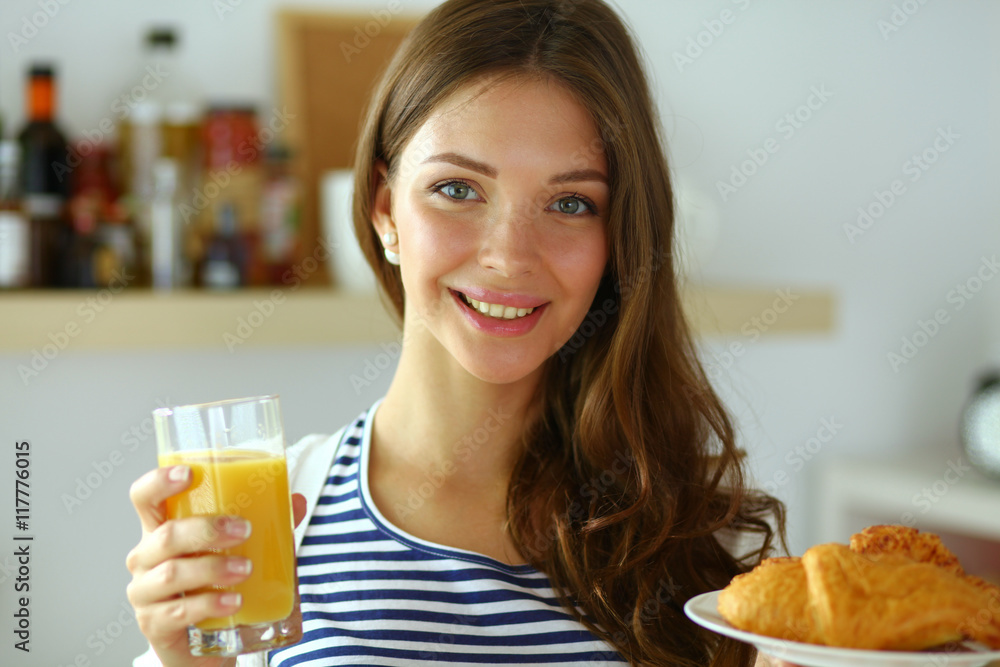 Young woman with glass of juice and cakes standing in kitchen . Young woman with glass of juice and cakes standing in kitchen .