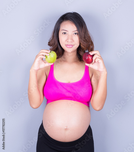 Beautiful pregnant woman with apple on gray background © geargodz