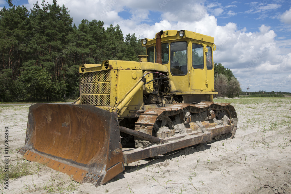 Жёлтый трактор на песке на фоне леса