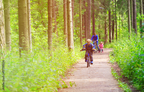 family sport - father and kids riding bikes in summer forest