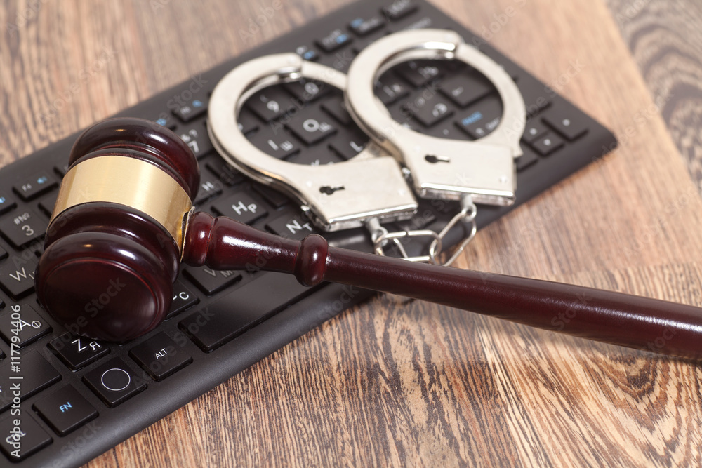 Computer keyboard,handcuffs and judge gavel on wooden background