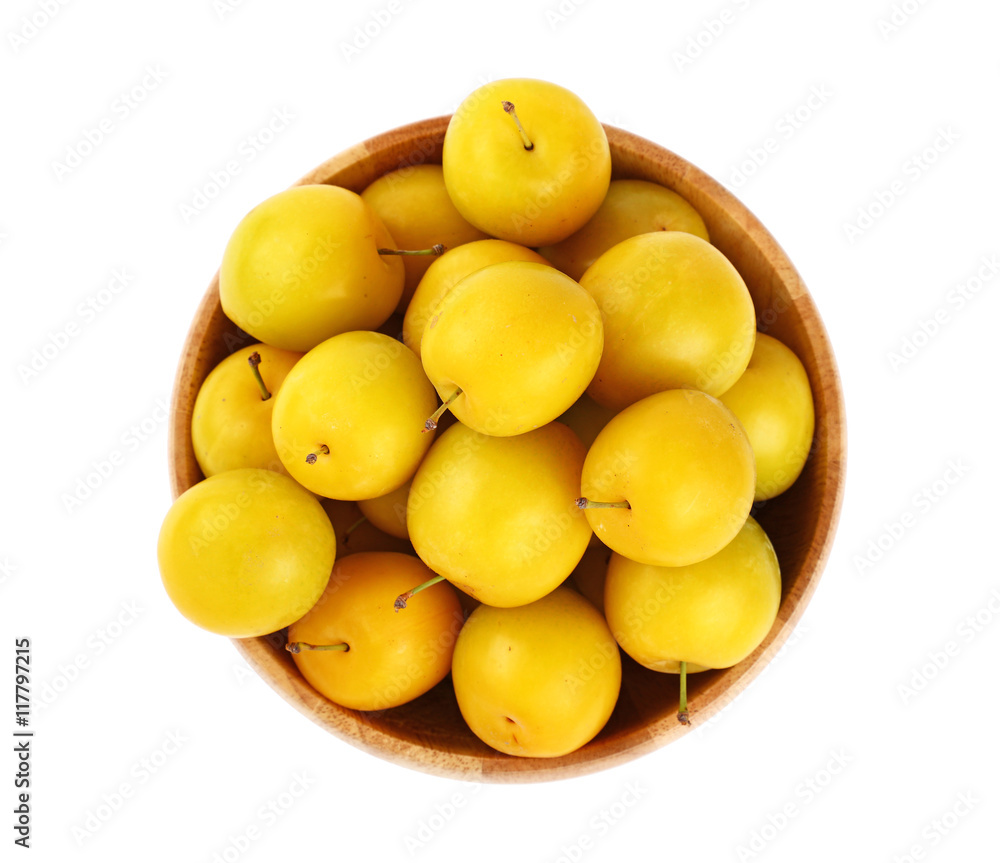 Fresh yellow plums in wooden bowl over white Fresh yellow plums in wooden bowl over white