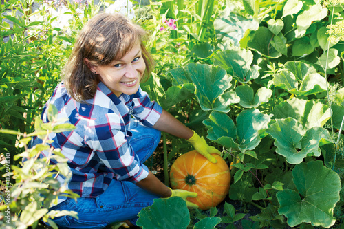 Woman gardener with orange pumpkin in the garden