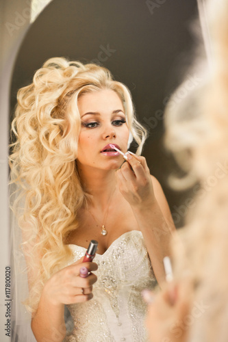 Blonde bride looks seductive painting her lips