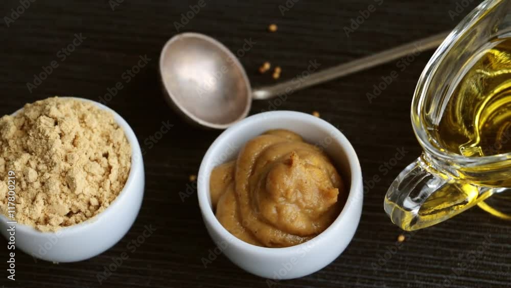 Set of different kinds of mustard - mustard seeds, mustard powder, french mustard, cremogenized and mustard oil - on black background. Slow pan. Set of different kinds of mustard - mustard seeds, mustard powder, french mustard, cremogenized and mustard oil - on black background. Slow pan.