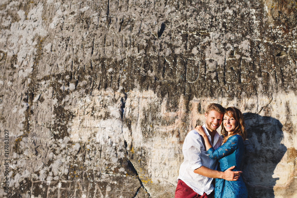 Happy embracing smiling couple near stone wall Happy embracing smiling couple near stone wall