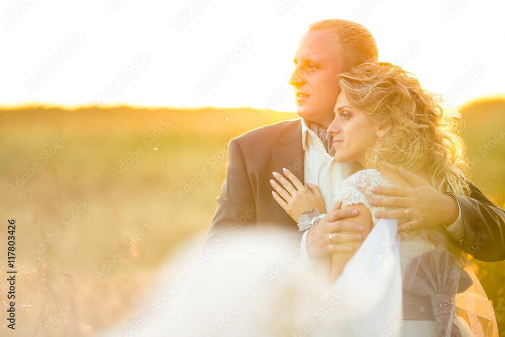 Gorgeous bride leans to a groom enjoying the sunset over the fie