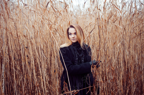 Portrait of young attractive woman in black coat and hat. Autumn landscape, dry grass