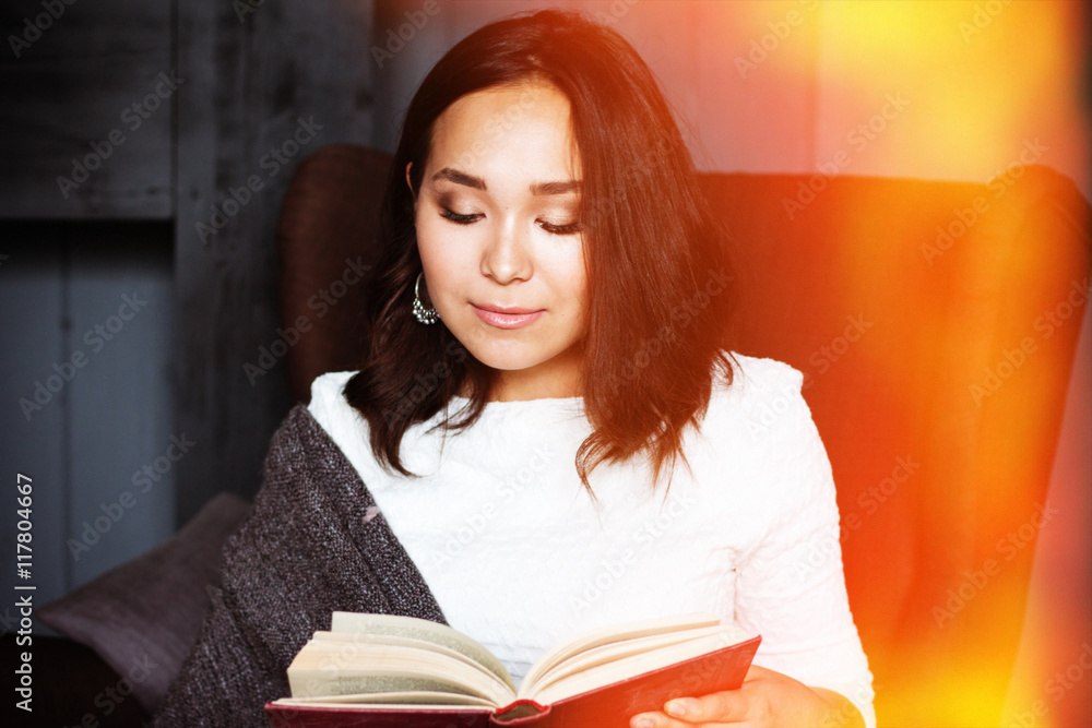 young,beautiful girl wrapped in warm plaid blanket reading book