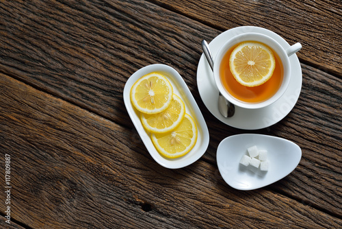 Top view of cup of tea with lemon and sugar cube on wooden table