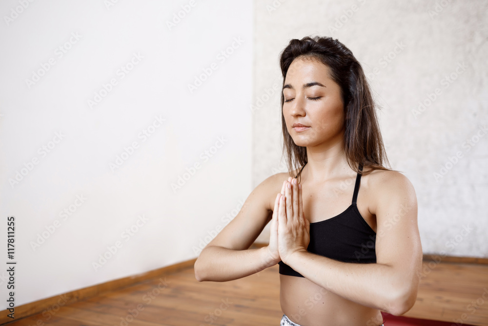 Close up portrait of young beautiful athletic girl practicing indoor yoga with closed eyes and palms in namaste gesture Close up portrait of young beautiful athletic girl practicing indoor yoga with closed eyes and palms in namaste gesture