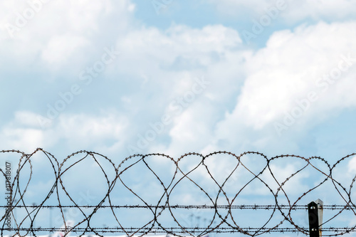 Closeup fence barbed wire with clouds sky background.