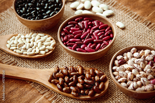 Beautiful multi-colored beans in bowls and wooden spoons on a background of burlap