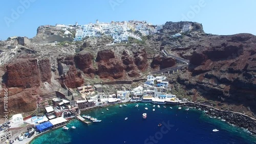 Aerial footage of Oia, Santorini - Famous white houses and blue domes on the edge of the cliff and blue lagoon.