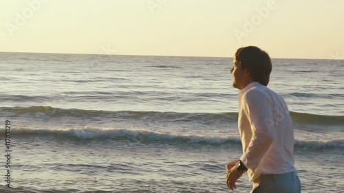 Young barefoot man running along the beach coastline at sunsetin yellow sunset rays photo