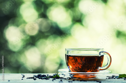 Cup of black tea on the open window on green blurred nature back