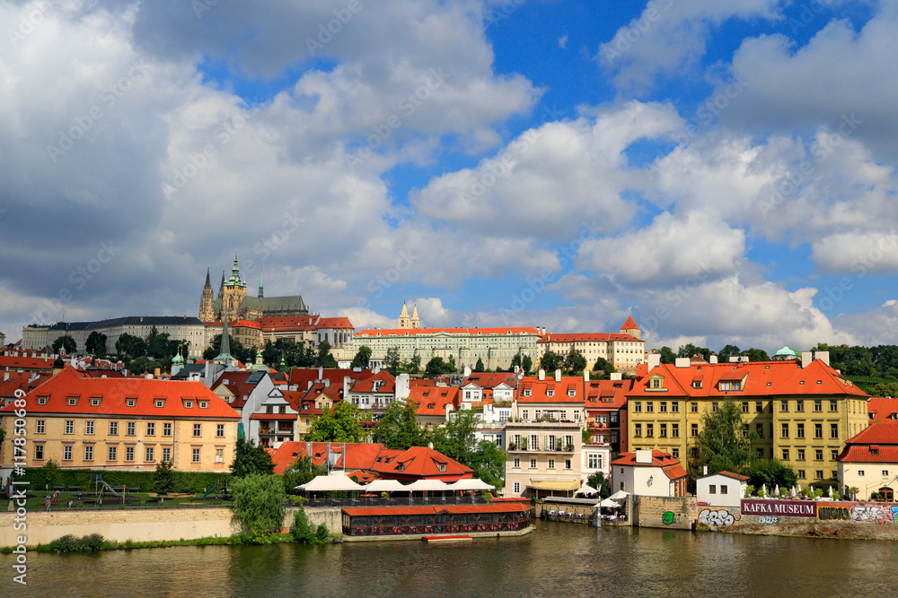 The Prague Castle, gothic style, largest ancient castle in the world and Charles Bridge, built in medieval times, moving boats, Summer view of Prague with blue sky with big white clouds. River Vltava.