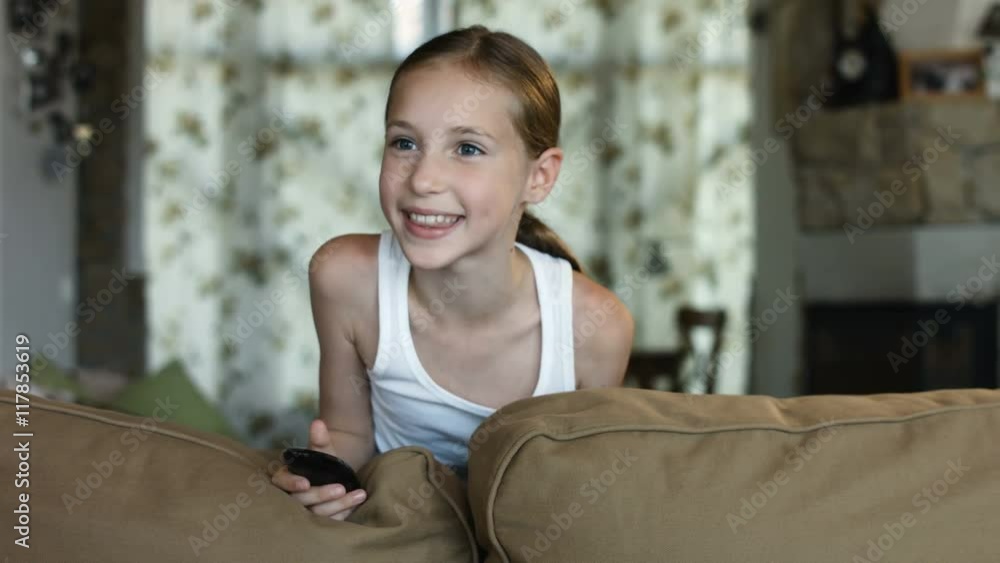 Child watching TV, little girl having fun on the couch, holding remote
