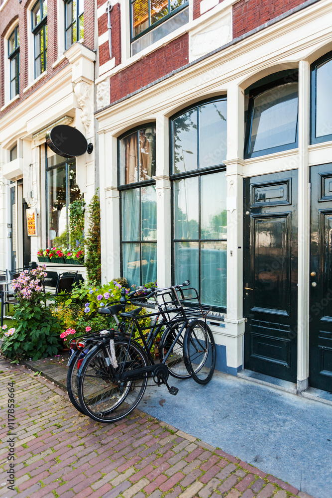 Fragment of colorful typical dutch building in Amsterdam with bicycles, standing near the entrance to the house and flowers in pots, Netherlands.