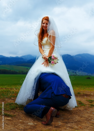 groom peeking under his bride dress - funny wedding concept. Stock Photo
