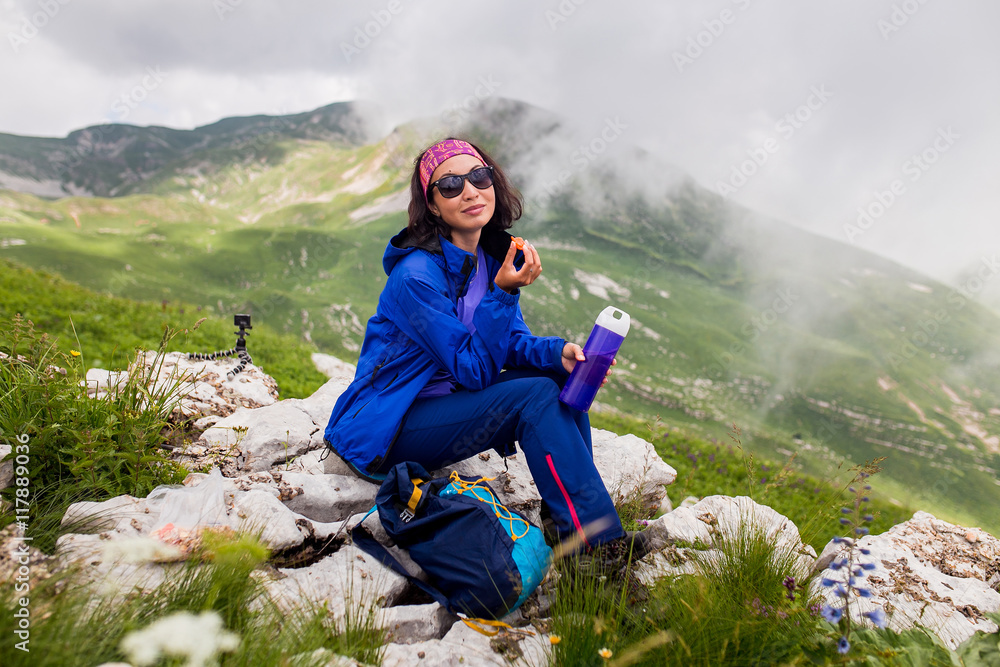 Female Hiker sitting and resting and using Thermos drinking Tea and Trail leading to high Peak on Background
