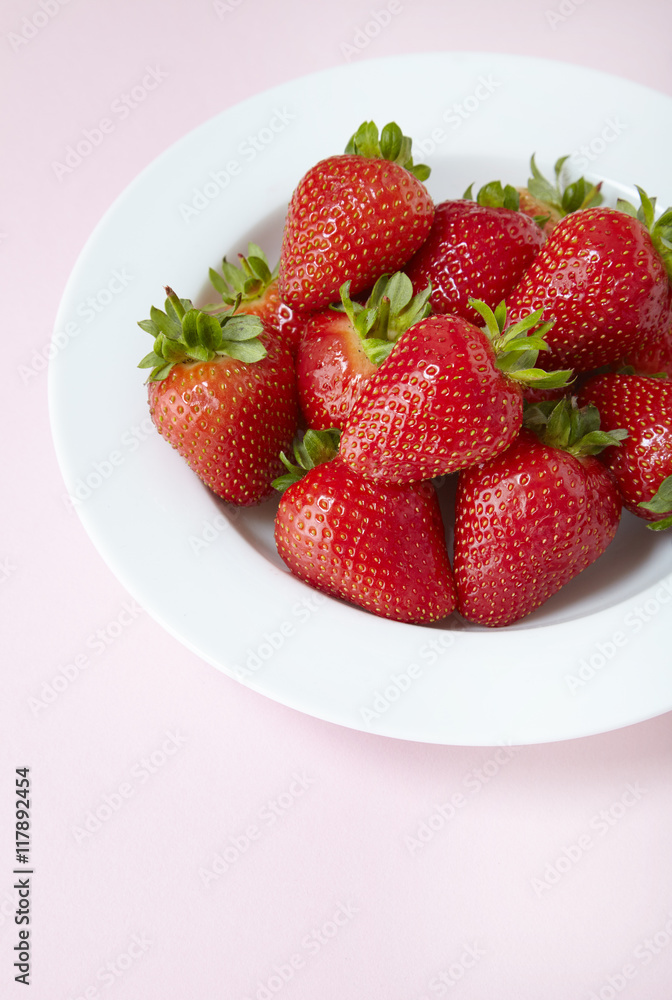 A bowl of fresh ripe strawberries on a pastel pink background A bowl of fresh ripe strawberries on a pastel pink background