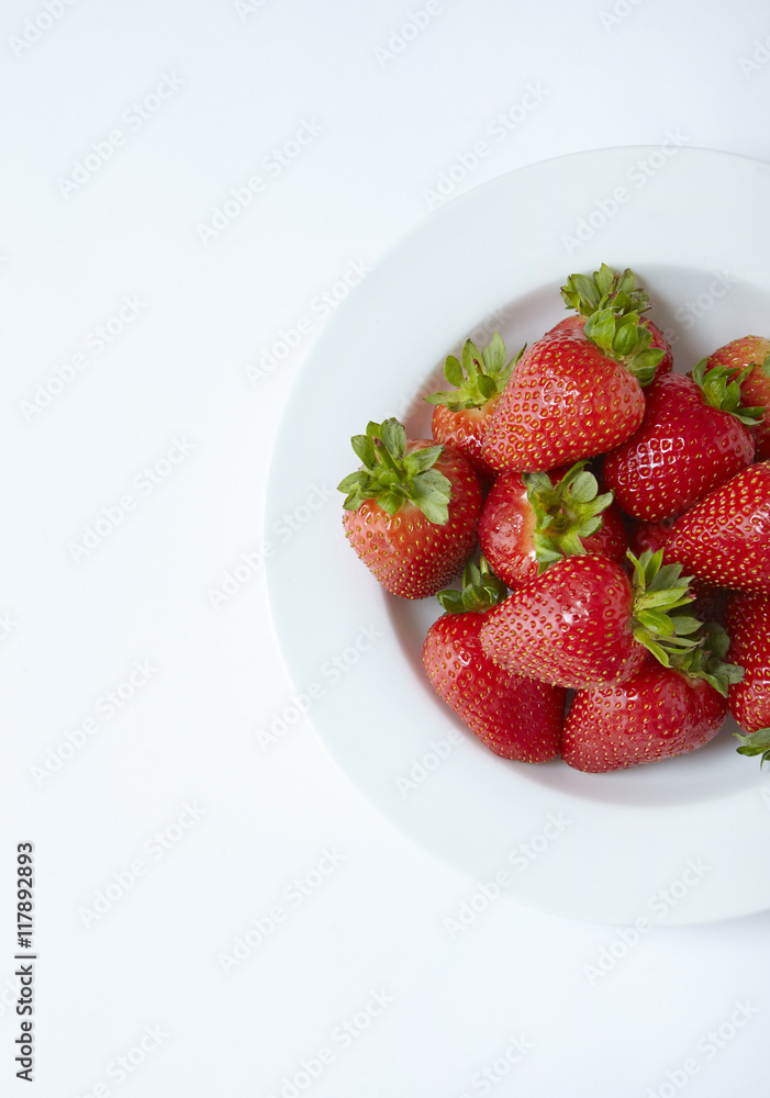 An aerial view of a bowl of whole ripe strawberries on an off white background An aerial view of a bowl of whole ripe strawberries on an off white background