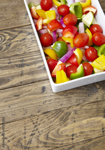 A serving dish of fresh  chopped Mediterranean vegetables on a rustic wooden table top background forming a page border