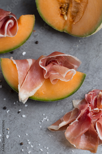 Ham mix. Jambon. Traditional Italian and Spanish salting, smoking, dry-cured dish - jamon Serrano and prosciutto crudo sliced with melon on grey background. Copy space. Closeup. 

