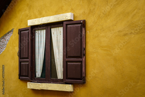 Wooden window with curtain on cracked yellow wall