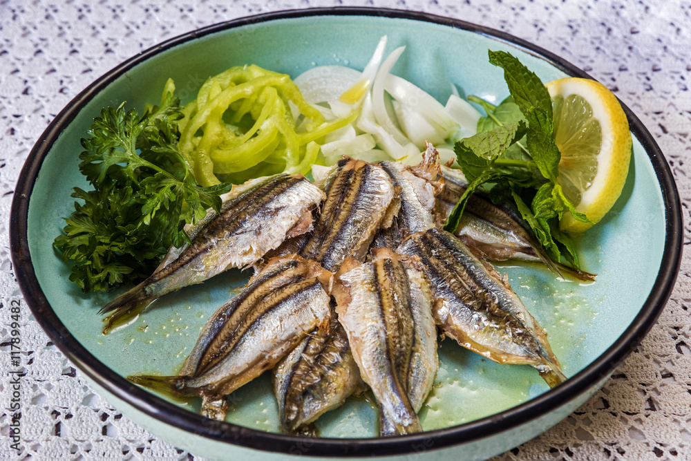 Cooked sardines with green salad in old-fashion plate on table