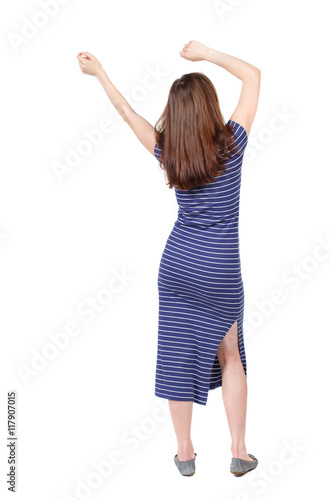 back view of dancing young beautiful woman. girl watching. Rear view people collection. backside view of person. Isolated over white background. The brunette in a blue striped dress waving his