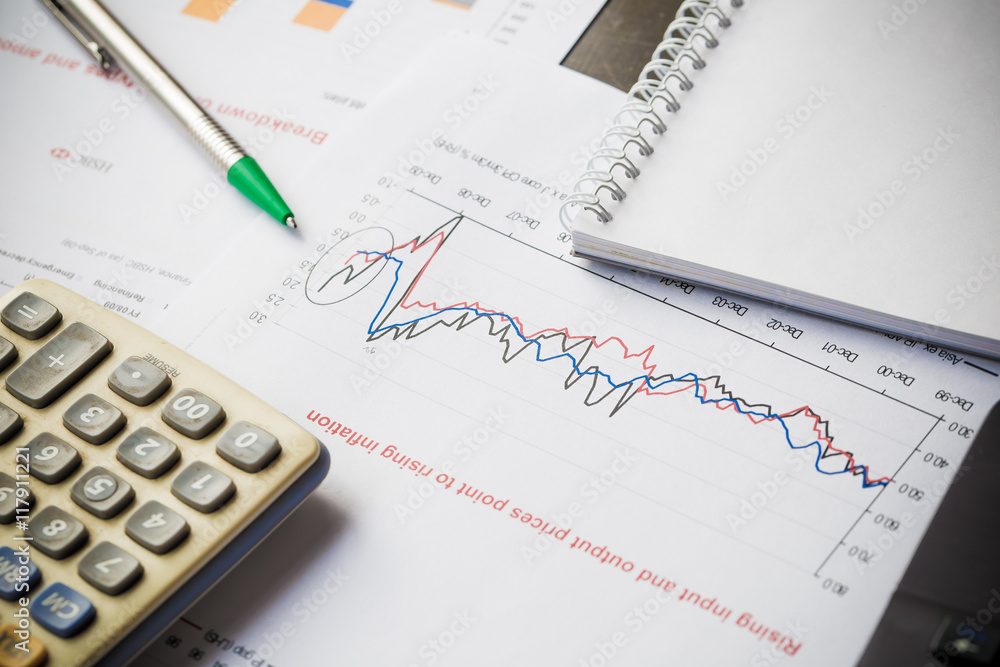 Papers with graphs data calculator and pen on wood table Papers with graphs data calculator and pen on wood table