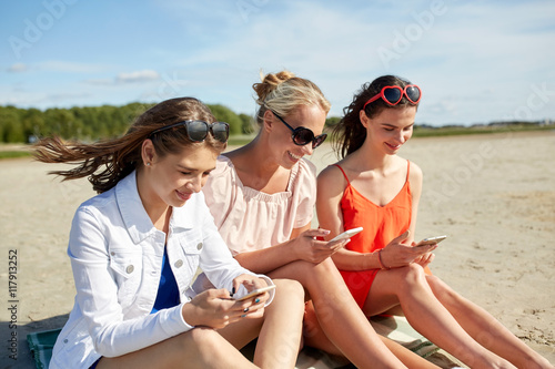 group of happy women with smartphones on beach © Syda Productions