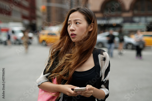 Young Asian woman in city texting cell phone 