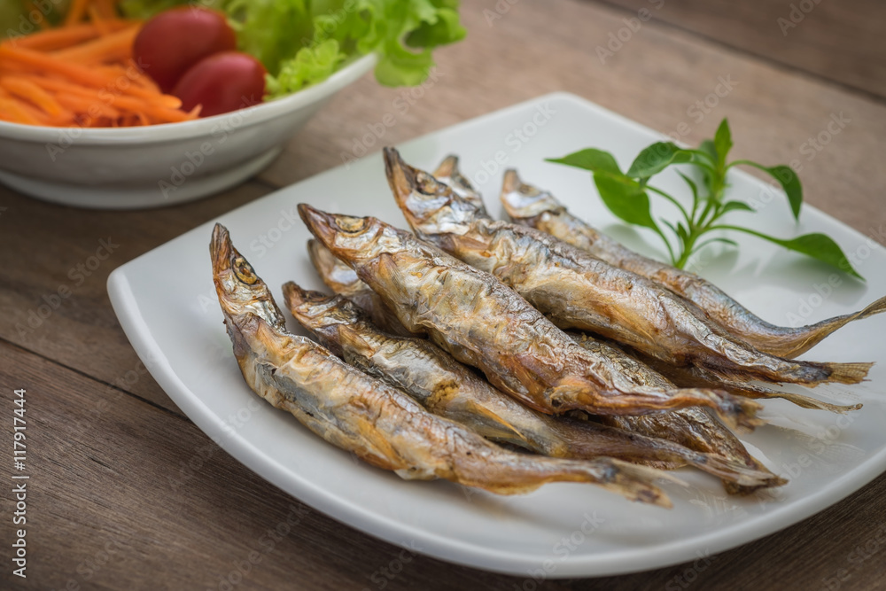 Grilled fish capelin or shishamo on plate and salad in bowl Grilled fish capelin or shishamo on plate and salad in bowl