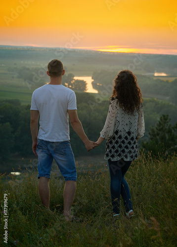 romantic couple looking into the distance at sunset on outdoor, beautiful landscape and bright yellow sky, love tenderness concept, young adult people