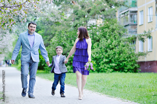 Family portrait. Mother, father and son walking holding hands. Spring. Full length.
