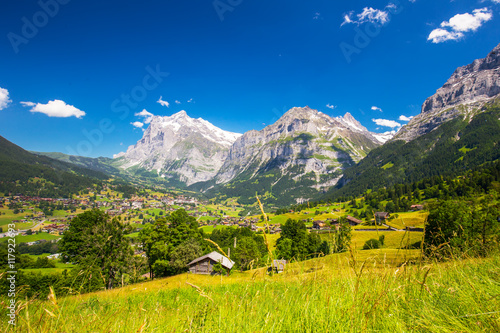 View to famous Grindelwald valley, green forest, Alps chalets and Swiss Alps (Schreckhorn, Berglistock and Wetterhorn) in the background, Berner Oberland, Switzerland, Europe. 