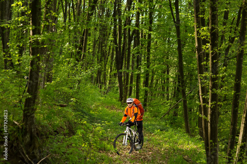 Biker in orange jersey on the forest road © Aleksey