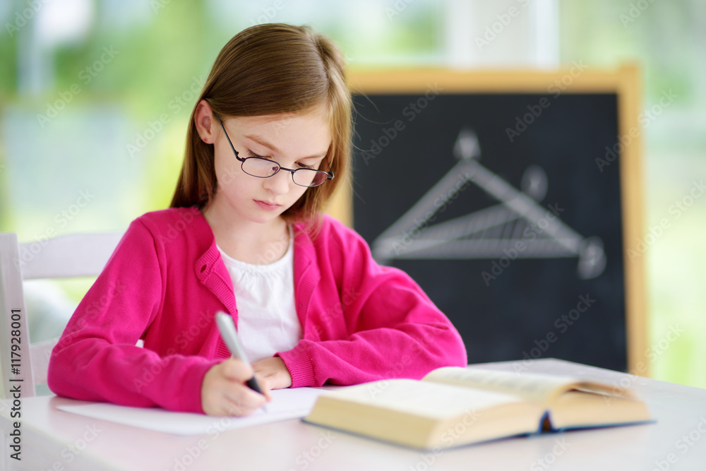 Smart little schoolgirl with pen and books writing a test in a classroom Smart little schoolgirl with pen and books writing a test in a classroom