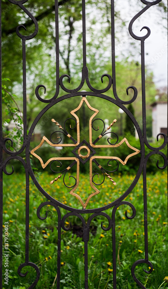 Intricate wrought iron church gate with golden cross on green background