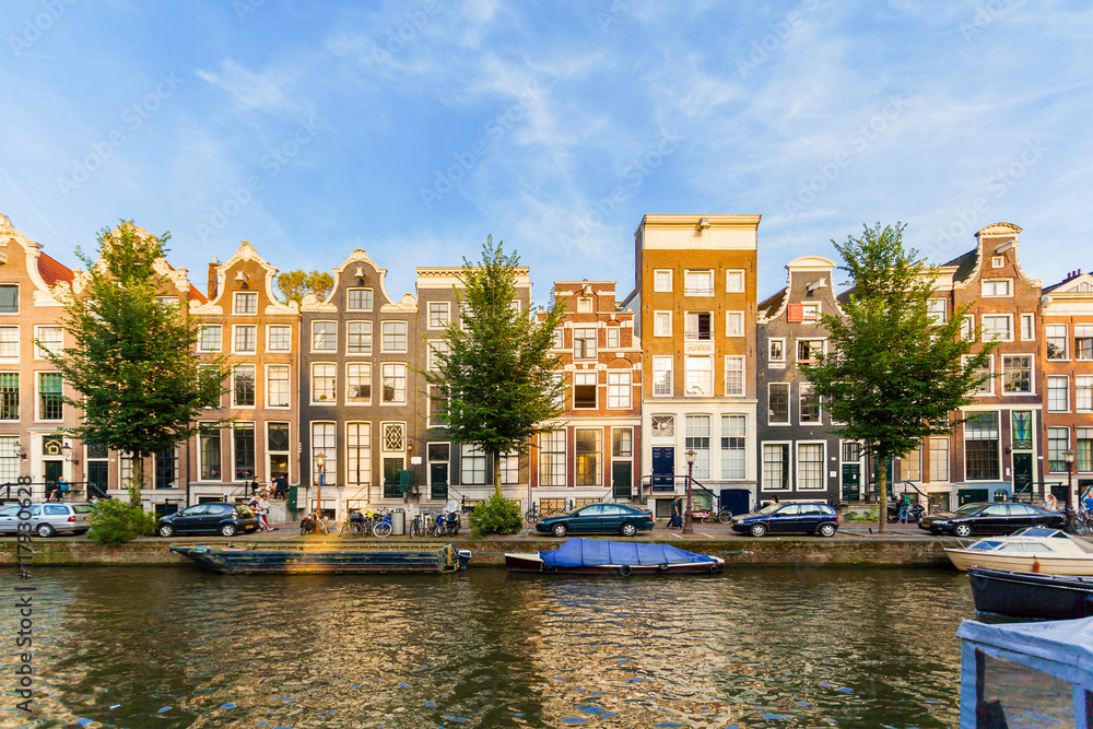 Typical street in Amsterdam with canal and colorful houses in the Dutch style on the Sunset. The buildings that stand in the water. Lifestyle. Netherlands.