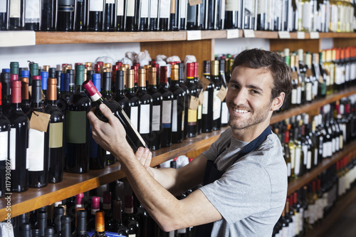 Smiling Salesman Arranging Wine Bottle On Shelf photo