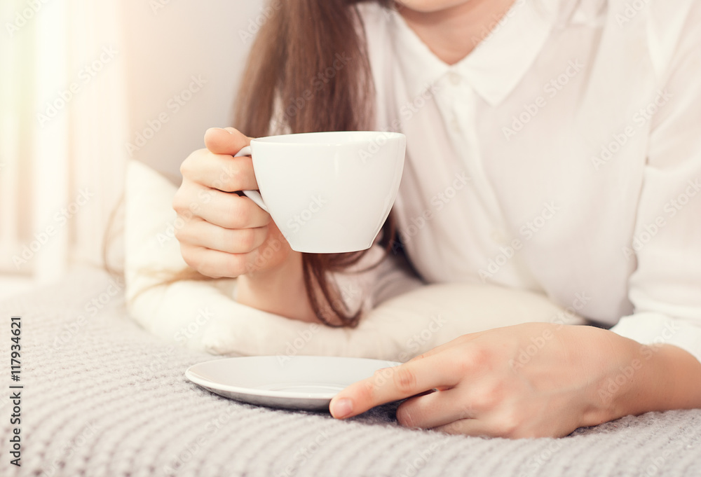 beautiful young woman hold cup of coffee lying think relaxing on the bed, bed home indoors, happy smile day dreaming with tea mug in hands looking up away in thought
